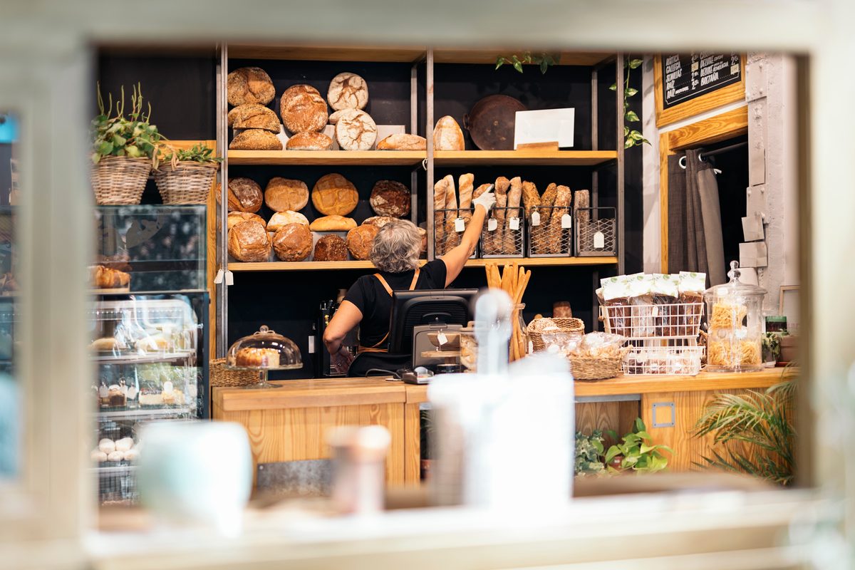 An Australian small-business owner reaching for fresh bread behind the counter of her bakery.