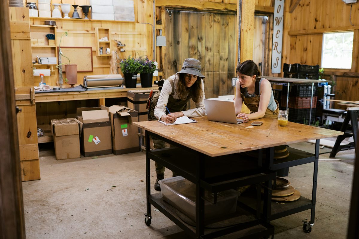 Two Australian small-business owners reviewing their books on a laptop in their workshop.